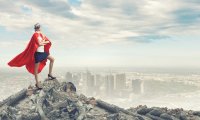 Individual in super hero cap standing on top of a mountain