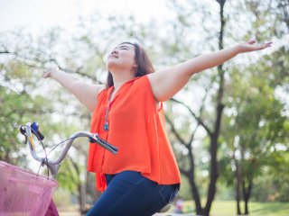 Pretty young girl on bicycle with arms oustretched with joy